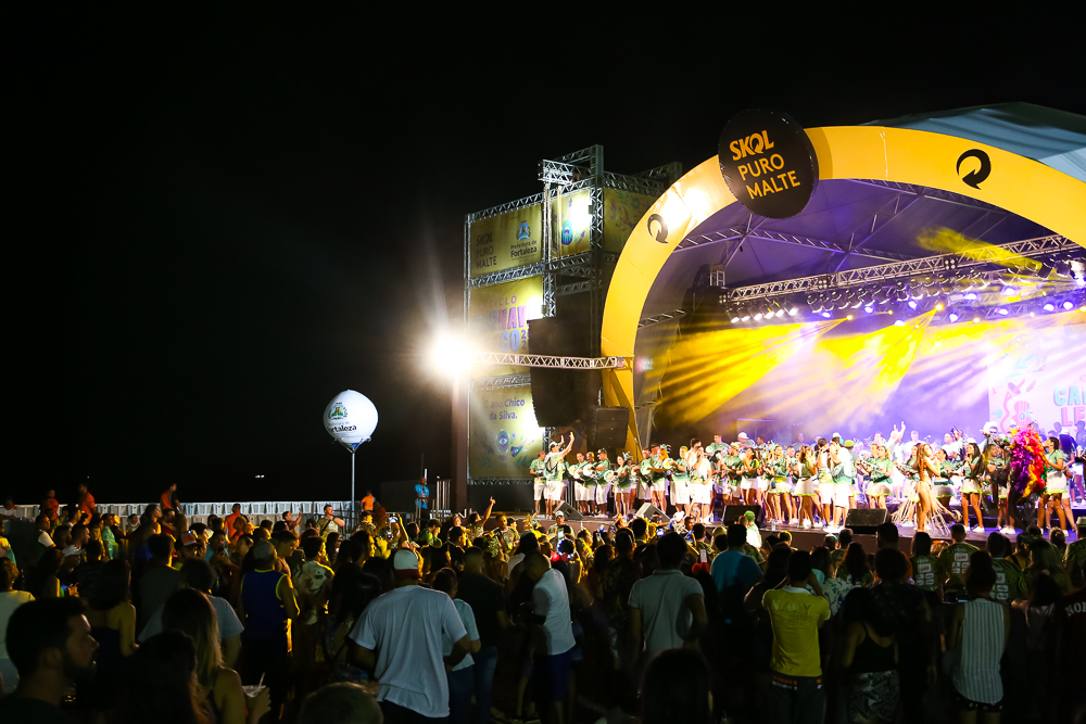 palco com banda se apresentando em cima e pessoas em baixo assistindo